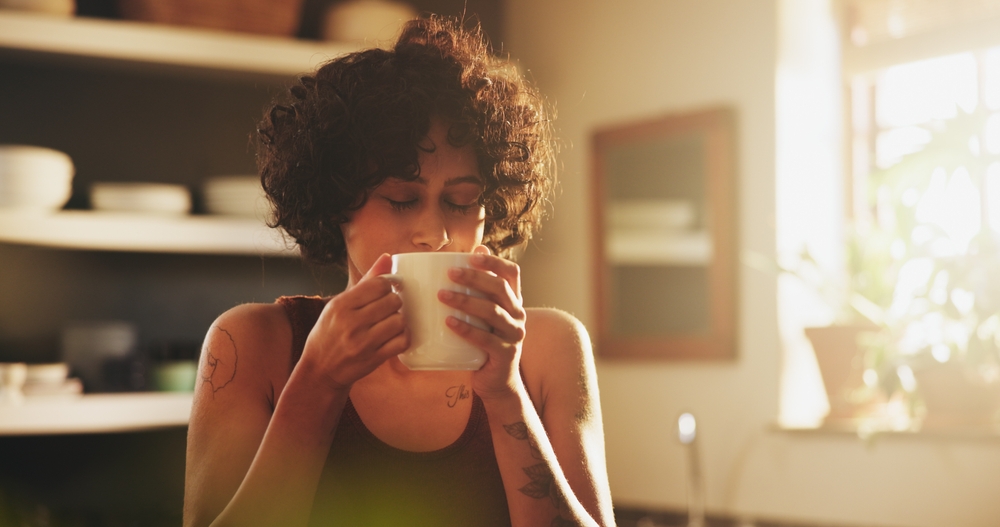 Woman, home and kitchen with cup of coffee on morning for breakfast, relax and enjoy. Female person, house and smile or satisfied with tea to chill, fun and day off with caffeine drink and peaceful