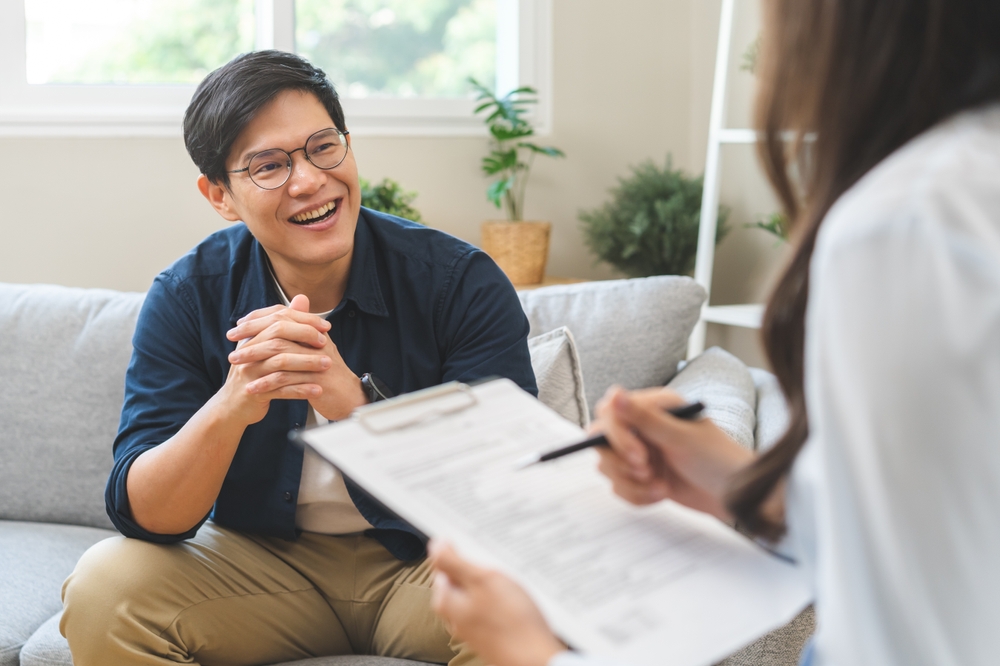 Psychology, depression. smile asian young male, man patient mental sitting on couch, explained symptom with psychologist, psychiatrist while doctor woman taking notes at clinic. Encouraging, therapy.