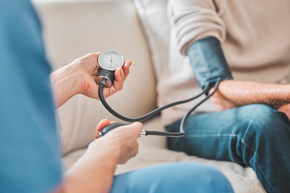 Nurse, elderly patient and blood pressure in house, retirement home and check up with medical professional. Monitor, hypertension and healthcare with pump for wellness, caregiver and people on sofa