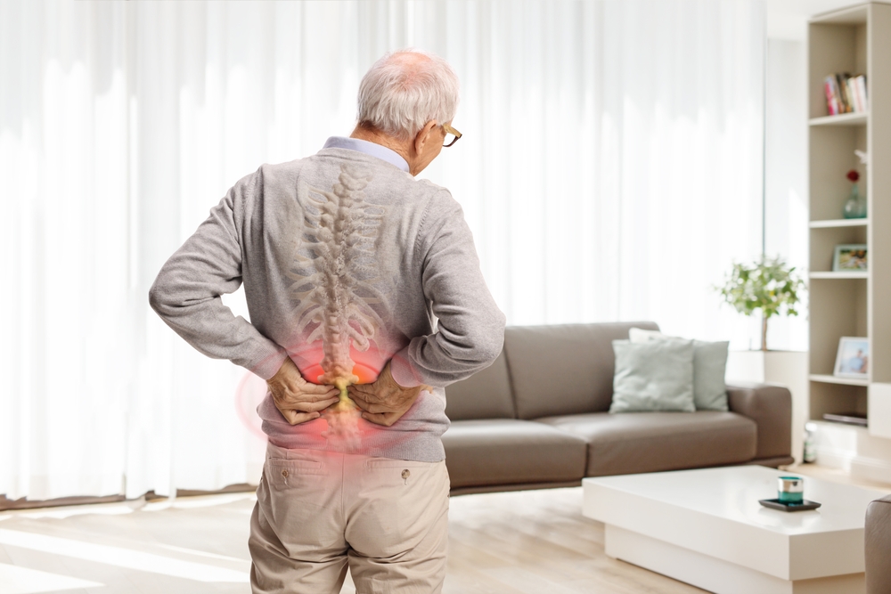 Rear view shot of an elderly man in pain holding his lower back with red painful spot