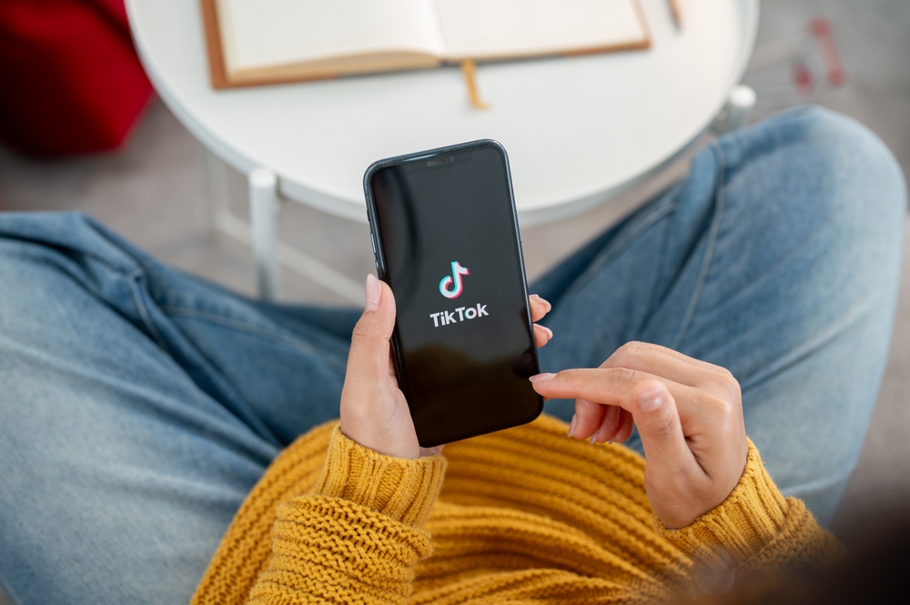 Chiang Mai, Thailand - Sep 19 2024: A close-up of a woman using the TikTok application on her iPhone while sitting on a couch at home. social media platform, mobile application, wireless technology