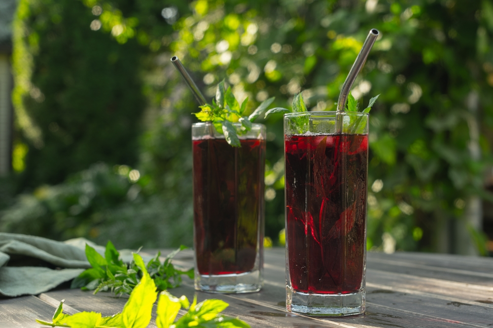 Summer cold tea. Two drinking glasses with red hibiscus tea decorated mint leaves.
