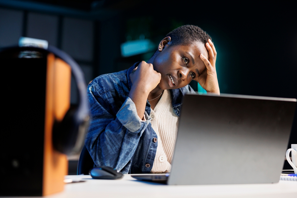 African American female freelancer looking stressed and frustrated as she uses her laptop. Black woman working at home appears tired and exhausted with headache while she browses on personal computer.