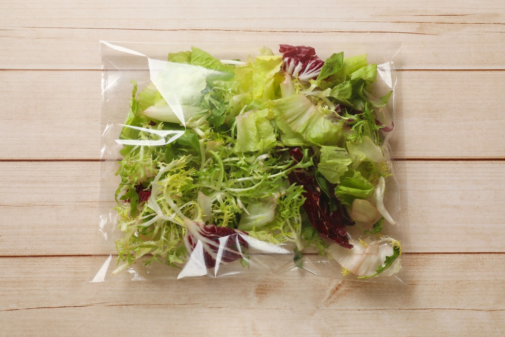 Pack of fresh salad mix on white wooden table, top view