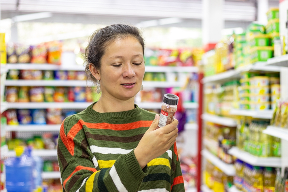 Customer selecting pink salt in a supermarket, holding the packaging while reading the label, carefully evaluating its benefits and making informed purchasing decisions