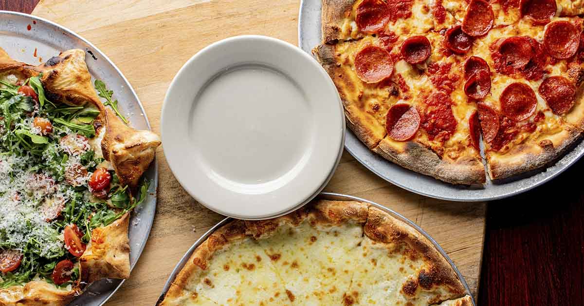 3 different types of pizza seen from above on a table with a single empty white plate in the middle