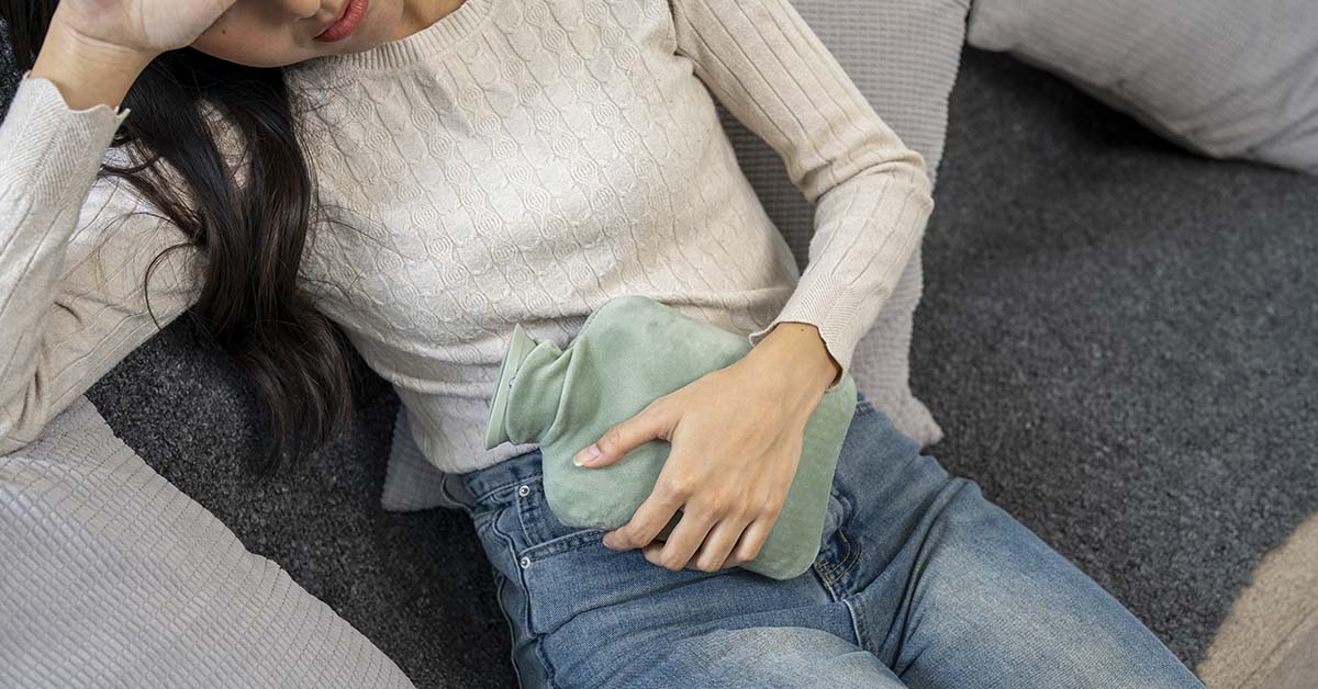 woman with water bottle placed over abdomen due to menstrual pain.