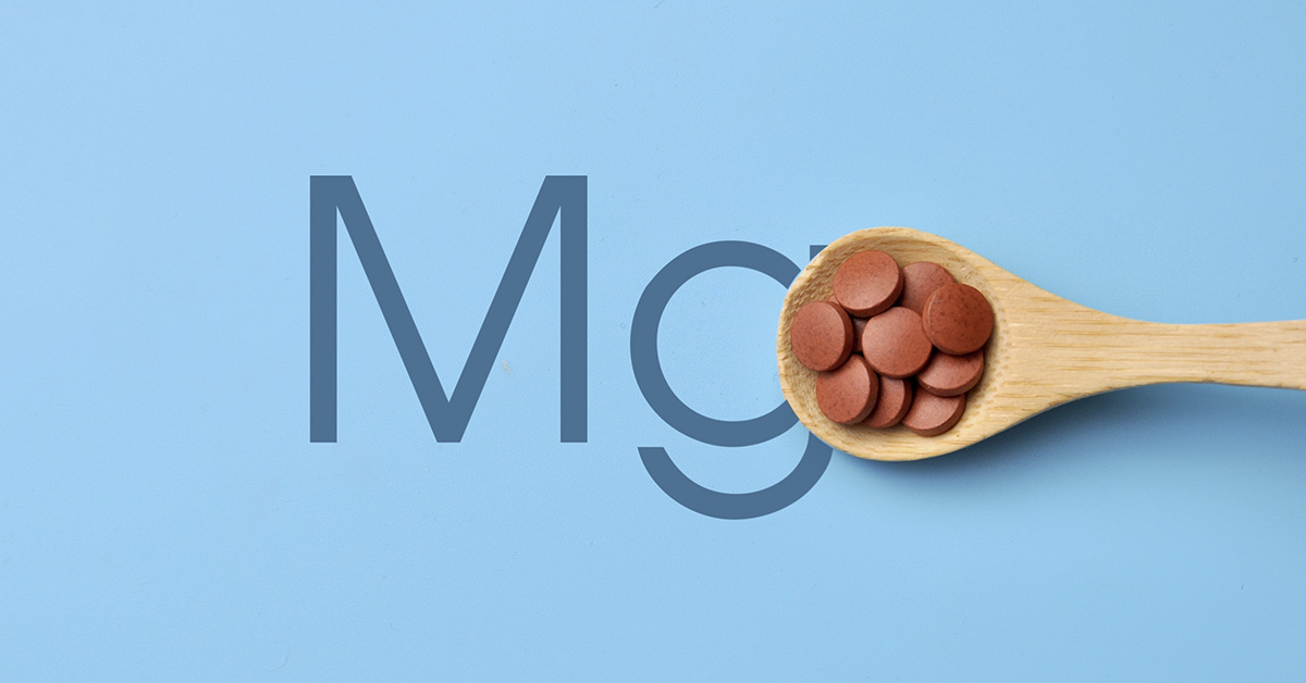 wooden spoon with small red supplement tablets with blue background with letters Mg indicating Magnesium.