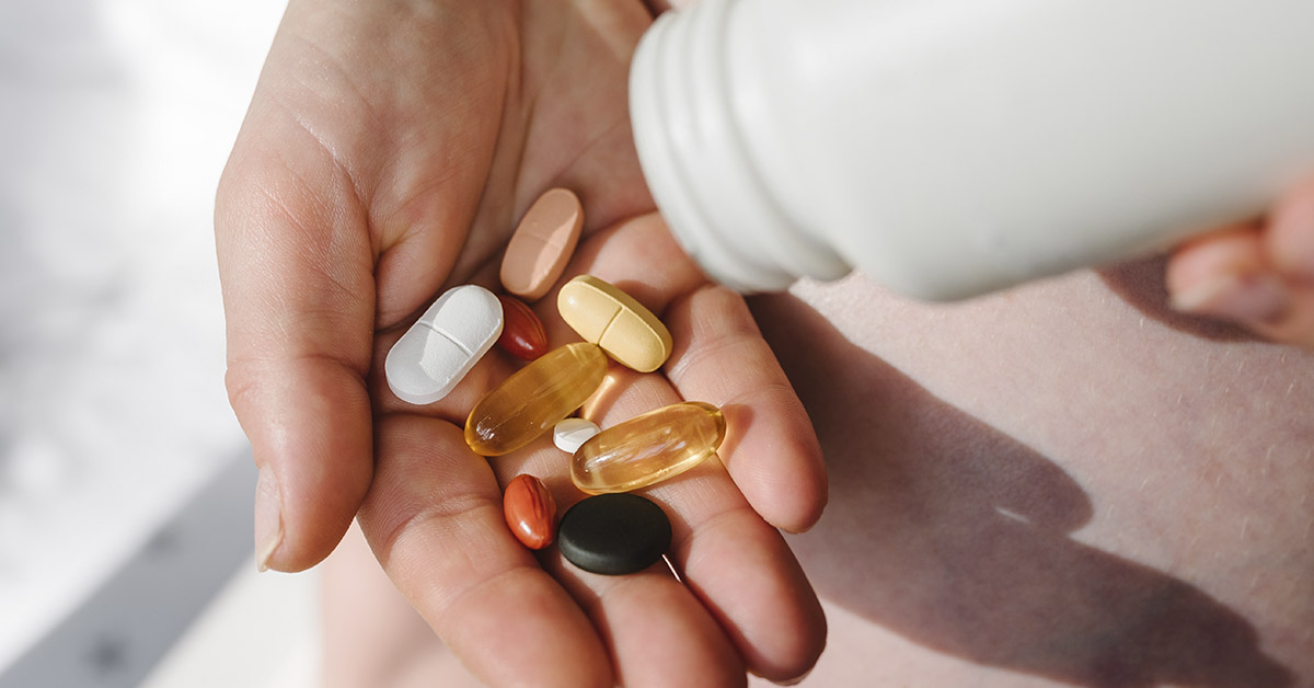 dietary supplements being dispensed from a white plastic bottle into the palm of somebody's hand