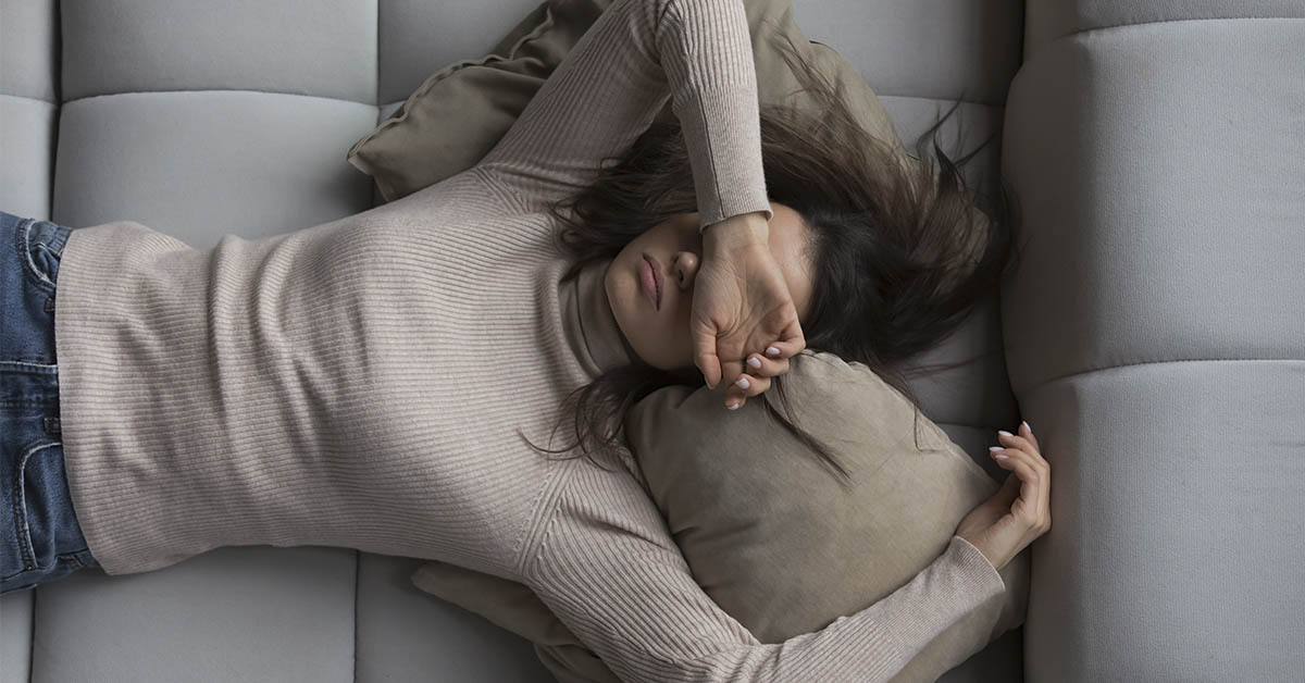woman laying on couch with arm across her face seen from above