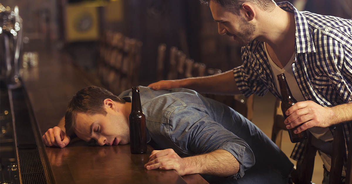 drunk man keeled over on a table being comforted by a friend
