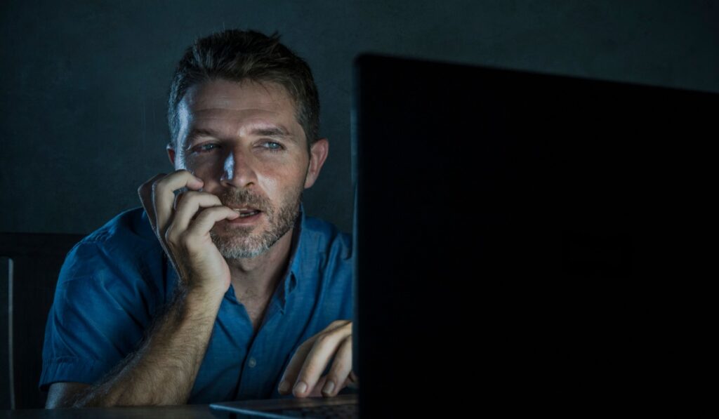 young aroused and excited sex addict man watching porn mobile online in laptop computer light night at home desk in pornography addiction and internet pornographic content concept
