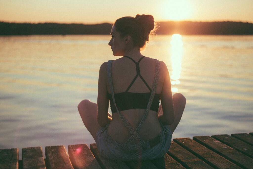 woman sits on a warf watching the calm water and sunset