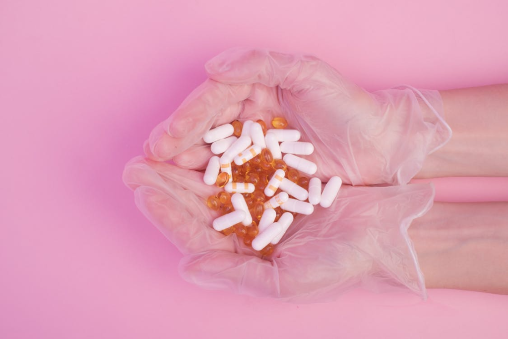 Crop pharmacist demonstrating heap of pills in pink studio

