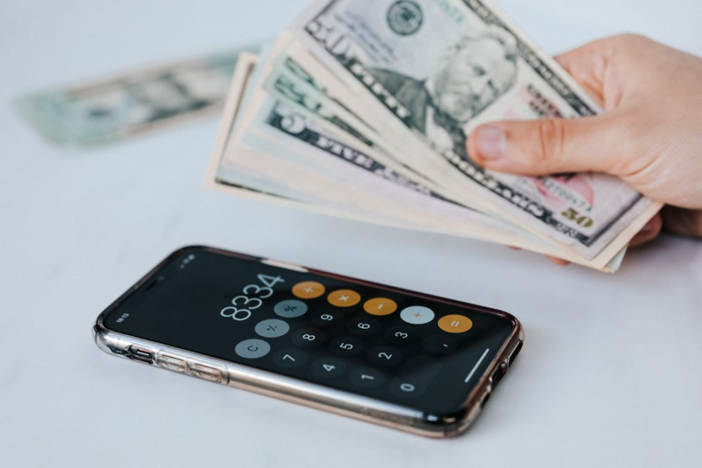 Crop faceless person with cash and calculator app on smartphone
