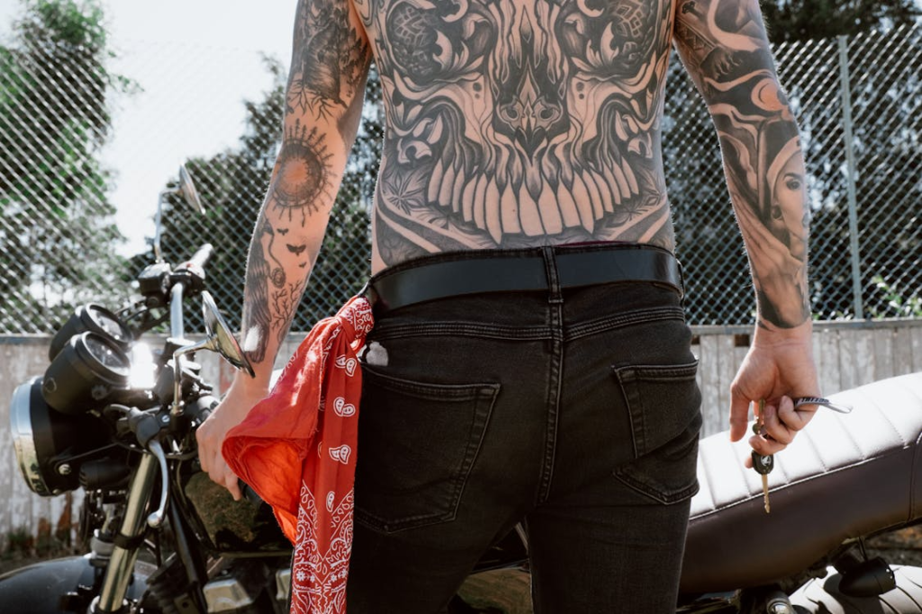 A Shirtless Tattoo Person Holding a Key in Front of a Motorbike
