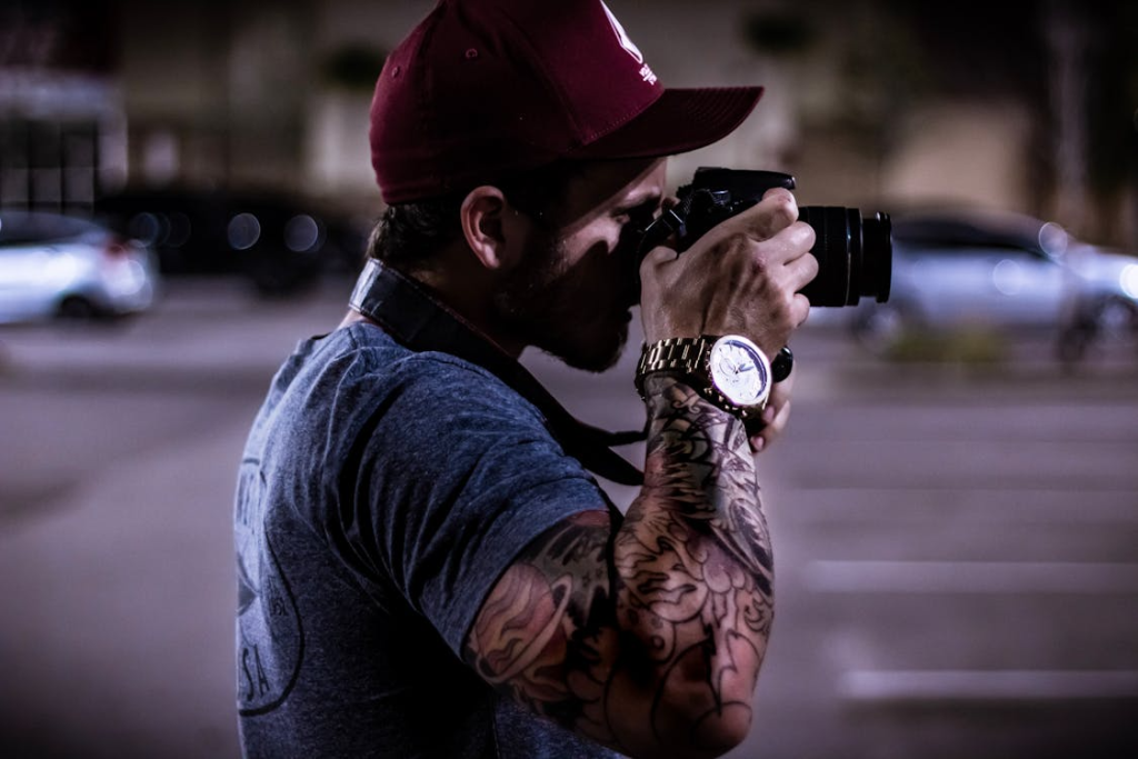 Man in Gray Tee Shirt Using Camera Standing Near Road
