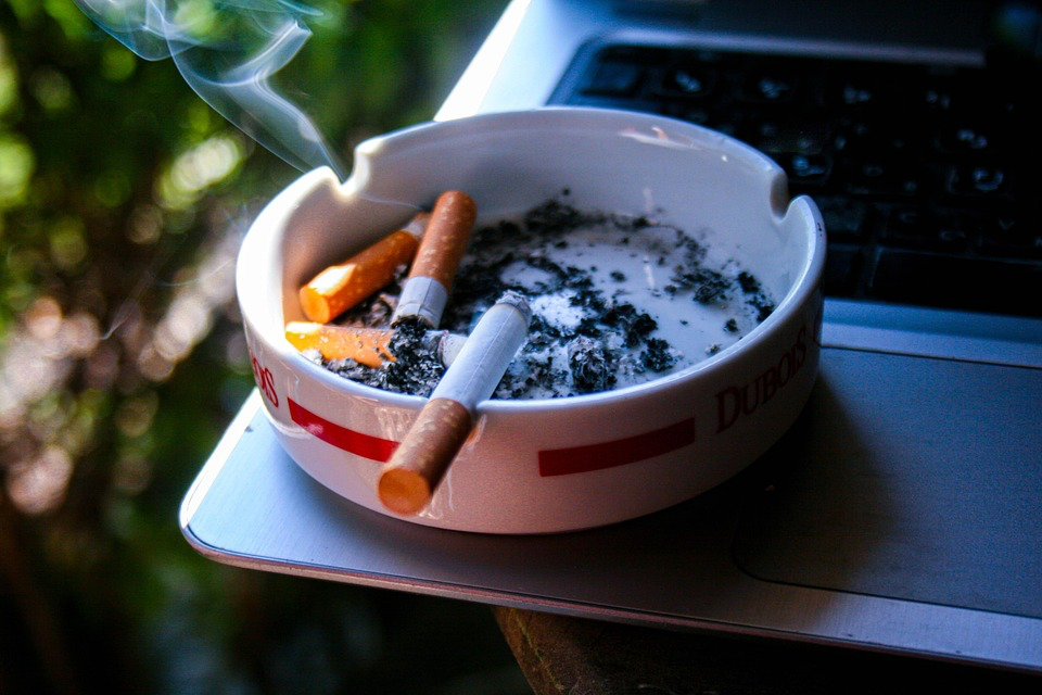 Ashtray with burning cigarettes and smoke.