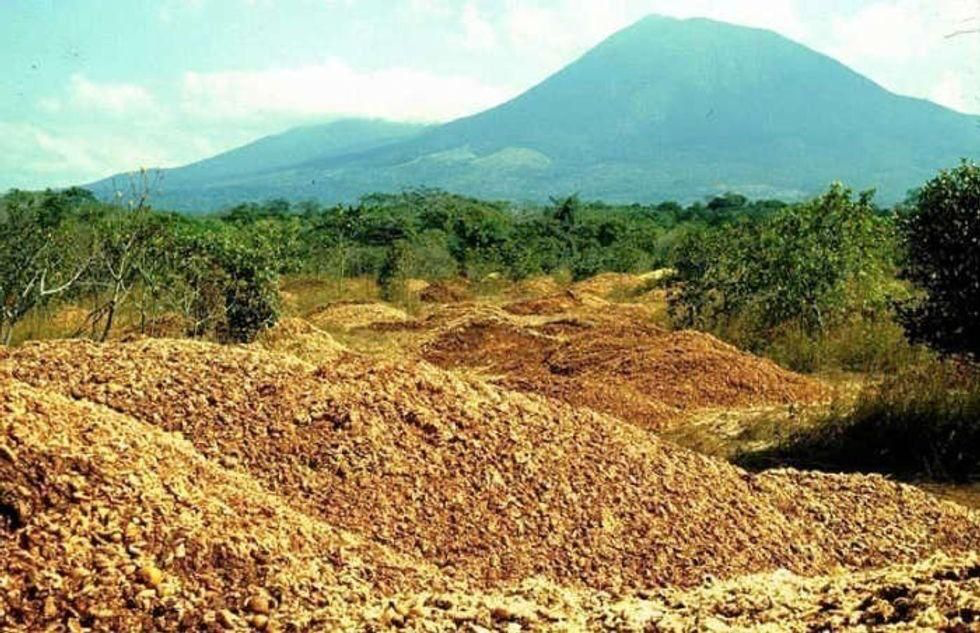 Massive piles of orange waste material dumped across the experimental site with mountains visible in the background.