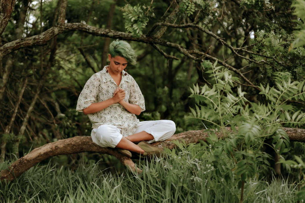 A Woman in Floral Shirt with Green Hair Looking Down while Sitting on a Tree Branch
