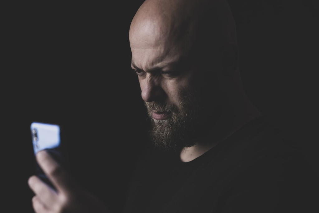 Person examining phone screen intently in low light while checking for hidden devices.