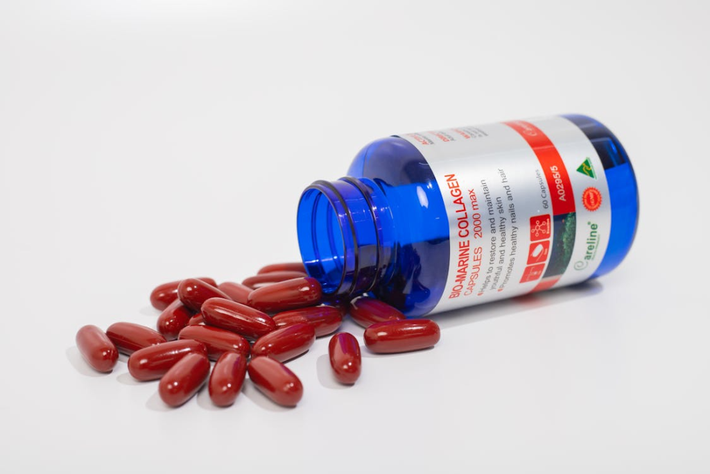 Red Capsules Spilling from Blue Bottle on White