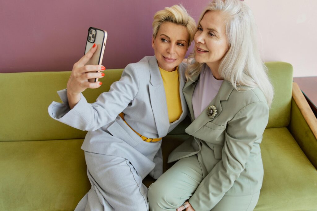 Woman in Gray Blazer Holding Iphone Beside Woman in Green Blazer 
