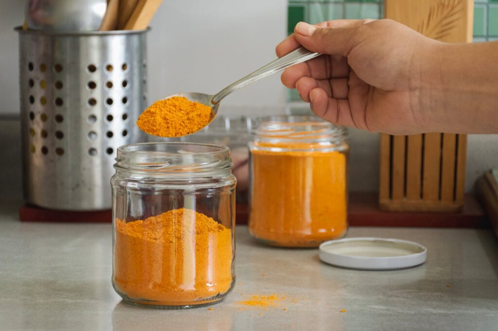 A person is holding a spoon over a jar of orange powder
