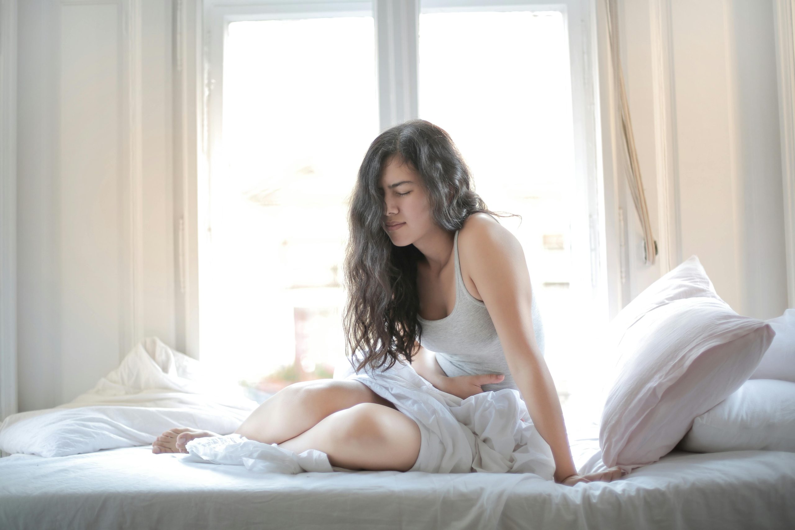 Woman sitting on bed, showing the pain of recurring urinary tract infections.