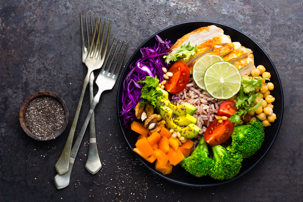 Buddha bowl dish with chicken fillet, brown rice, avocado, pepper, tomato, broccoli, red cabbage, chickpea, fresh lettuce salad, pine nuts and walnuts. Healthy balanced eating. Top view