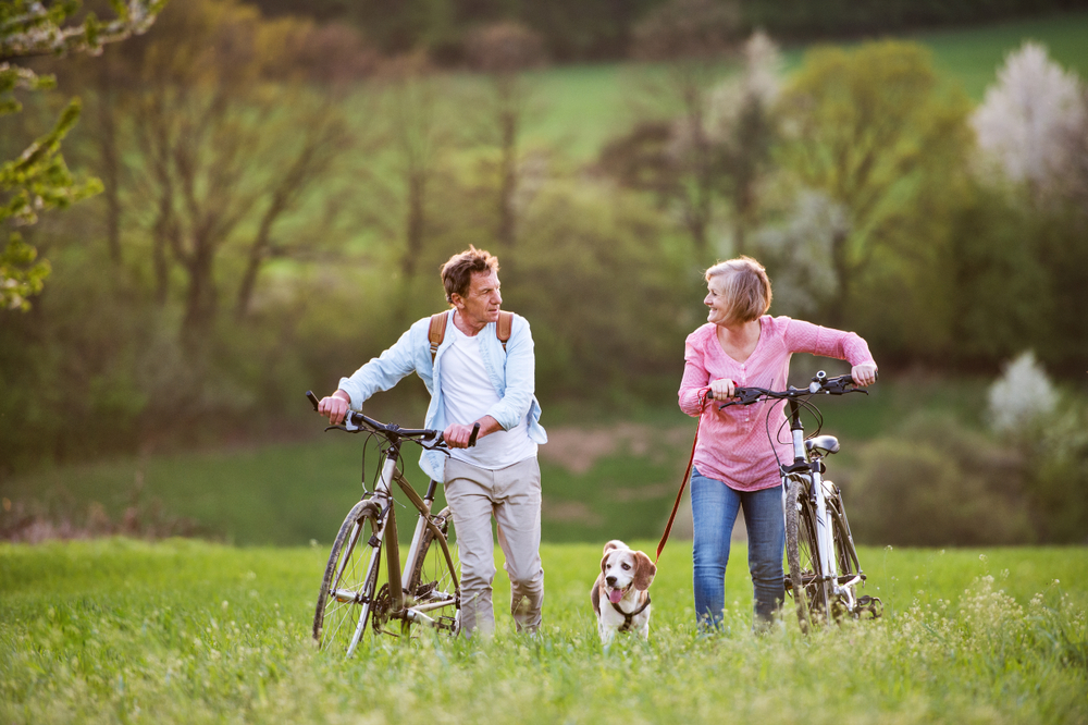 Beautiful senior couple with bicycles and dog outside in spring nature.