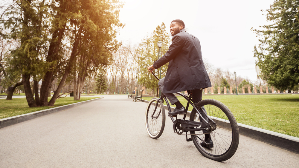 Gas savings concept. Young businessman riding bicycle to work in park, free space
