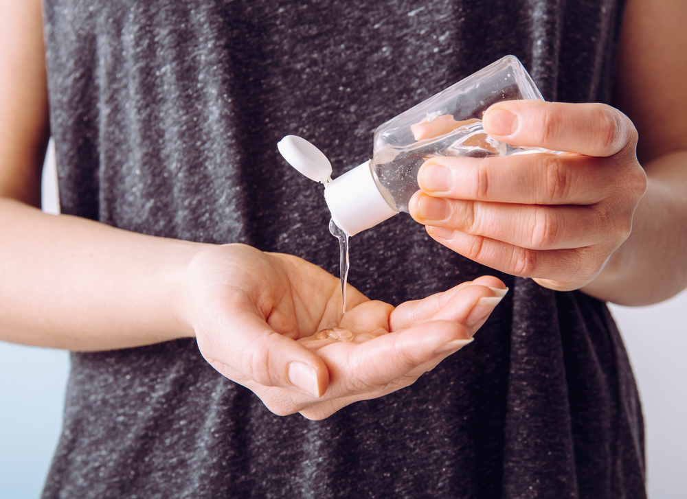 Close up view of woman person using small portable antibacterial hand sanitizer on hands.
