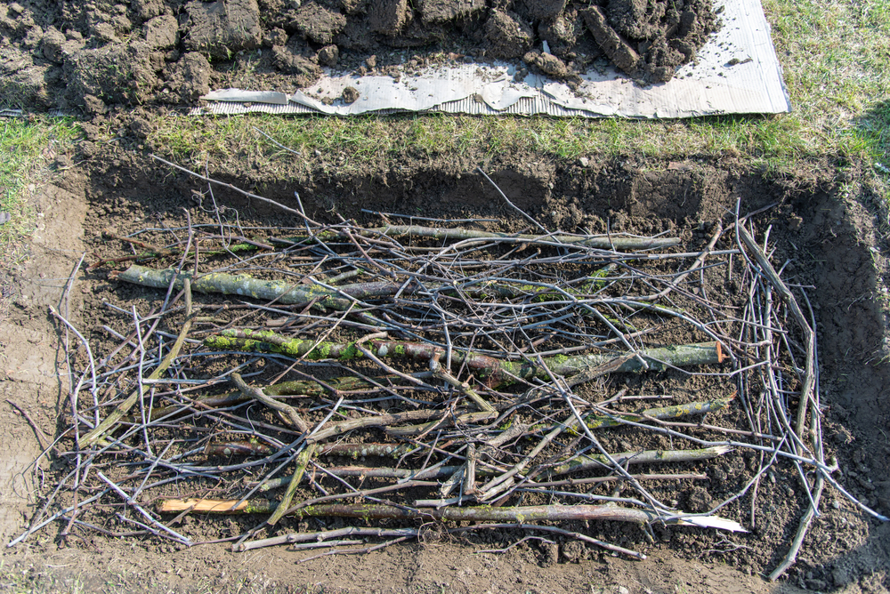 A high angle shot of twigs and logs laid on the ground for hugelkultur raised beds