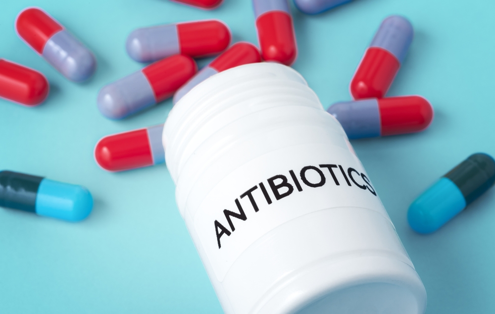 Antibiotic medicine concept, antibiotics bottle with pills spilled out, closeup on blue background