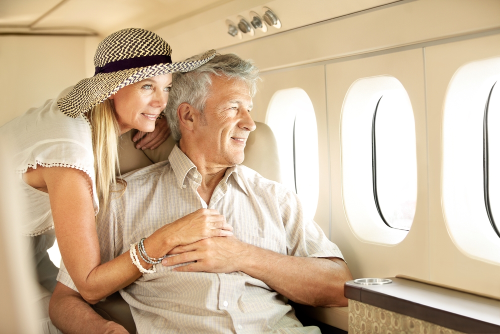 Taking a luxury trip. Smiling senior couple on an airplane looking out the window.