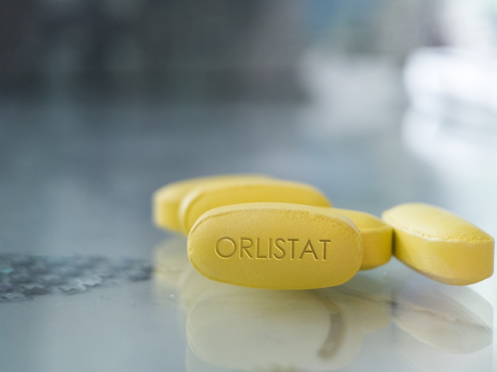 Orlistat yellow pill on glass background drug medication designed to treat obesity and prevent absorption of fats from human diets by acting as a lipase inhibitor