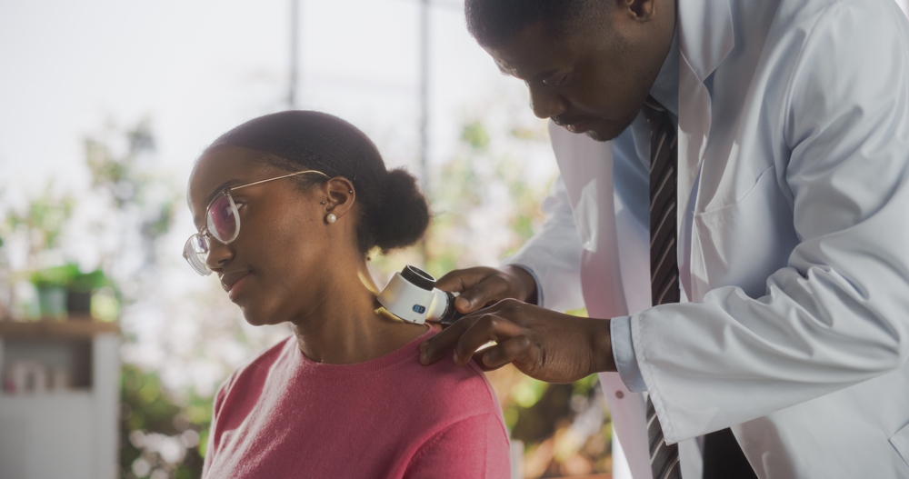 African Skin Care Professional Using a Dermatoscope to Examine Neck Tissue on the Skin of an Attractive Young Black Female During a Health Check Visit to a Clinic
