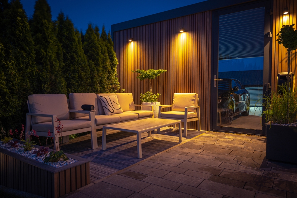 Lounge and Dining Area at Modern Residential Backyard Decorated with Outdoor Lights, Plants, Garden Table and Chairs. Cozy Summer Evening.
