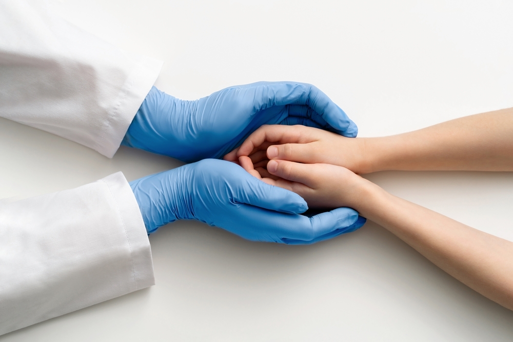 The doctor's gloved hands hold the child's hands. Medical concept.