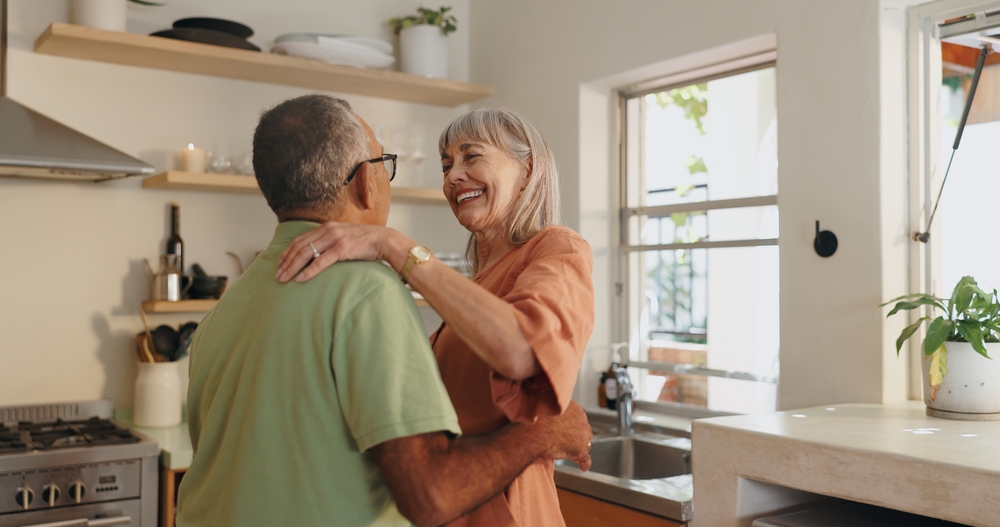 Senior couple, love and dancing in kitchen for retirement and healthy relationship with romance. Interracial marriage, old man and woman with dance steps in home for support and happiness together