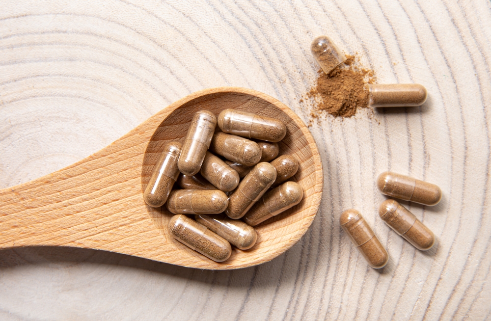 Withania somnifera known as ashwagandha. Ashwagandha root powder supplement capsules on wood spoon, studio shot.
