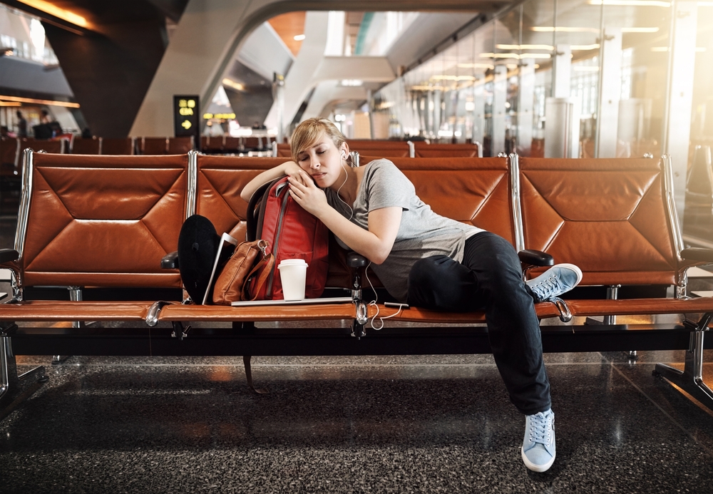 Woman, sleeping or waiting room with earphones at airport for flight delay, departure or jet lag. Young, tired female person or tourist asleep with luggage or headphones at terminal in travel station