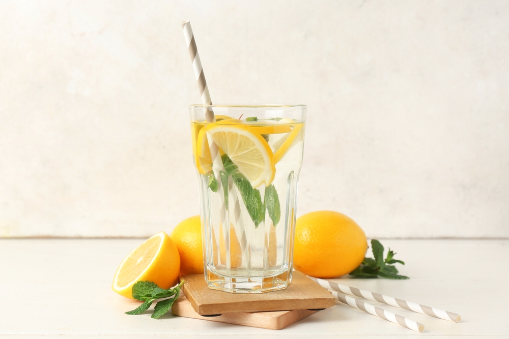 Glass of water with lemons, mint leaves and straws on light background
