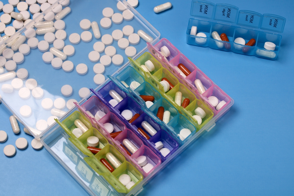 Colorful weekly and daily pill organizer boxes filled with various medicine capsules and tablets, promoting medication management and adherence