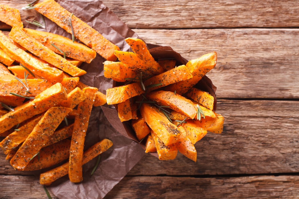 roasted sweet potatoes with herbs in a paper cone closeup on the table. Horizontal view from above
