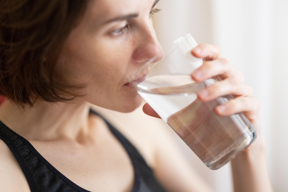 Person drinking from clear glass, emphasizing hydration as key prevention strategy.