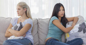 The One Major Sign a Friendship is Dead and How to Move On friends sitting on a couch sitting away from each other. Friendship in conflict concept