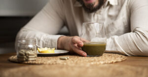 Warning Issued After Man Dies from Popular ‘Natural’ Supplement Kratom consumption concept: male bearded hipster holds a ready to drink glass of green liquid, powdered kratom melted in hot water, kratom tea, close up photo, selective focus