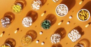 Top 10 Vitamins and Nutrients to Keep in Your Medicine Cabinet in 2025 various dietary supplements in small jars on an orange surface seen from above.